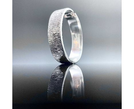 A 1970's hallmarked silver hinged bangle with textured finish, Birmingham 1973, weight 25.5g.