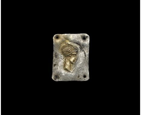  1st century BC. A rectangular parcel-gilt silver appliqué with mounting hole to each corner, stamped profile bust of a godde