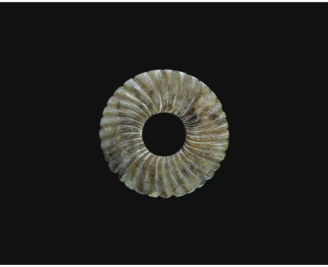  19th-20th century AD. A carved nephrite jade pendant, annular with notched edge and raised radiating ribs to each face. 19 g