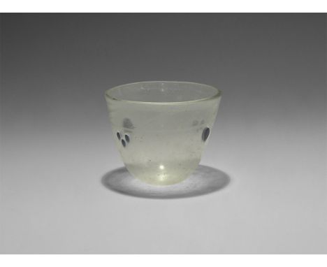  4th-5th century AD. A glass beaker or cup with slightly flattened base and flared rim, two sets of three applied blue-glass 