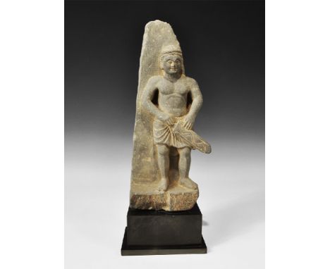  3rd-5th century AD. A carved schist frieze fragment depicting a standing kilted guard, bare-chested with right hand resting 