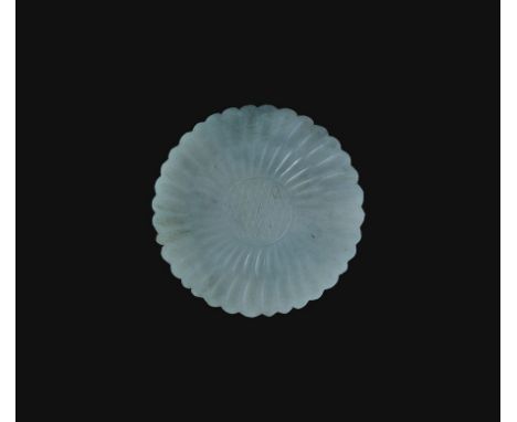  19th-20th century AD. A carved jadeite disc with notched rim, low-relief hatched centre and radiating petals. 41 grams, 57mm