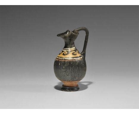  4th century BC. A miniature ceramic blackware oinochoe with fluted body, waisted neck, pedestal foot, pinched trefoil rim an