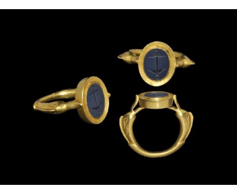 3rd-5th century AD. A carinated gold hoop with shoulders formed as opposed dolphins supporting a discoid plaque in their mout