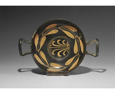  4th century BC. A ceramic blackware kylix with low pedestal foot, broad bowl, two square handles; to the exterior, two paint