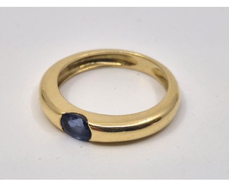 A yellow metal and single sapphire ring, flush set mixed oval cut single sapphire to centre, (yellow metal assessed as 18ct. 