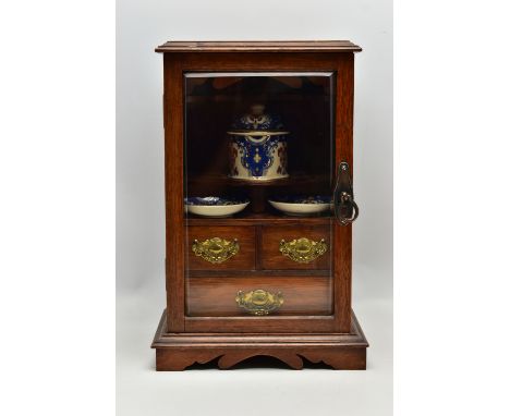 A LATE VICTORIAN OAK CASED SMOKERS CABINET, the bevel edged glazed door opening to reveal a pipe rack, shelves holding a pott