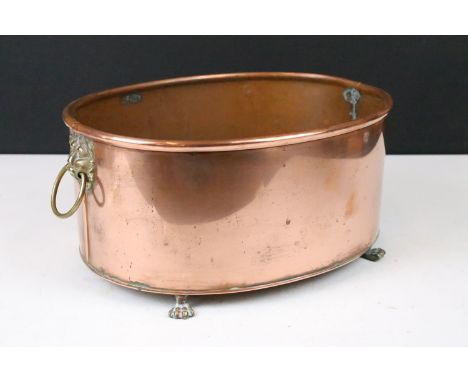Copper oval planter with rolled rim, brass lion mask drop ring handles and raised on four brass paw feet, 30cm long x 14cm hi