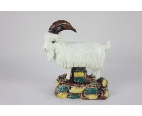 A glazed pottery model of a goat possibly Irish, standing on a base of coloured cobble stones, 18cm