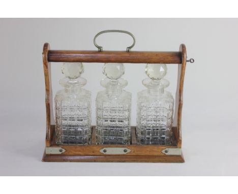 A Victorian oak three decanter tantalus with metal mounts and carry handle, lock and key, on plinth base, a/f (small chip to 