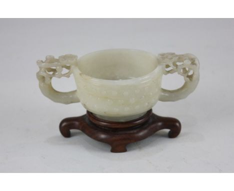 A Chinese jade two handled cup, with a rounded bowl carved with studded decoration, the two handles pierced and worked in the