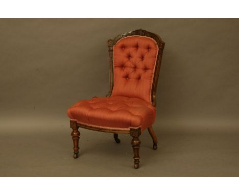 A late Victorian walnut salon chair, with buttoned spoon back above stuff over seat, in red fabric, on turned supports