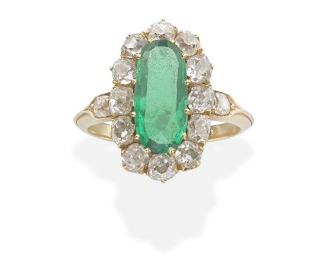 EMERALD AND DIAMOND CLUSTER RINGThe oval-cut emerald within a cushion-shaped diamond surround, between similarly-cut diamond 