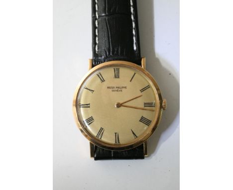 A fine quality 18ct gold gents Patek Philippe Geneve watch with gold tone face presenting roman numerals, mounted on a black 