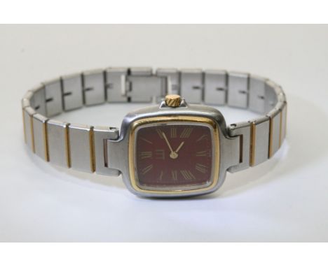 A box containing an Alfred Dunhill ladies white meal and gold tone wrist watch with a deep red face and roman numerals
