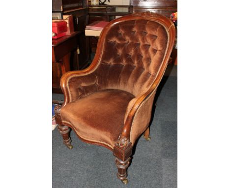 An Edwardian mahogany framed button back armchair with brown velvet upholstery on turned legs and castors