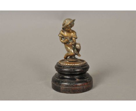 An Edwardian cast metal figural mascot, in the form of a seated child holding a mallet and chisel, raised on a stepped turned