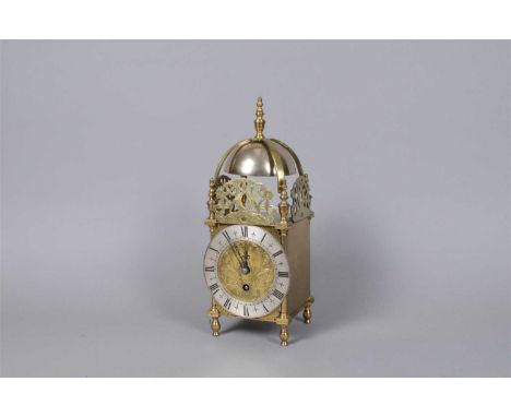 A reproduction brass cased lantern clock, with pierced mounts above a silvered disk dial populated with black Roman numerals,