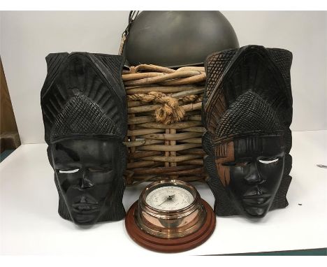 A basket containing two African masks a barometer and a ceiling light.