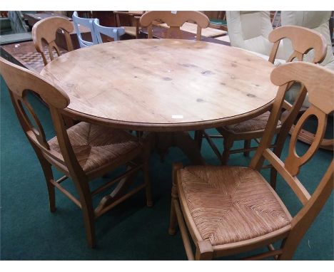 A large circular pine tripod table and five chairs with rush seat pads.