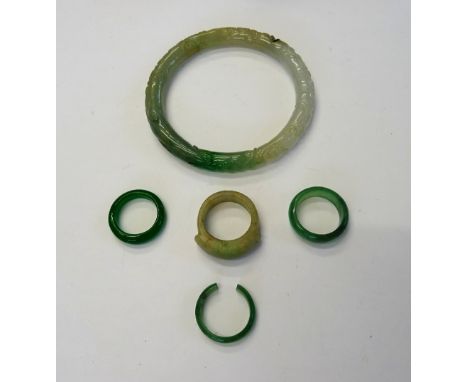 A carved jade circular bangle, with floral and scrolling decoration, a jade ring, of saddle form, a pale green stone band rin