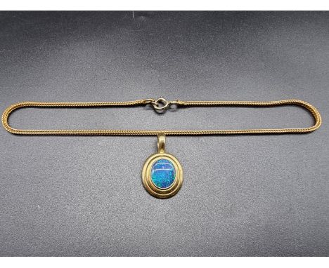 A yellow metal oval pendant set cabochon dark opal, stamped 750, 35mm high, on a gold plated chain. 