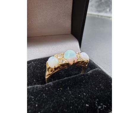 A yellow metal ring, set three oval cabochon opals and four small mine cut diamonds, size O, gross weight 3g. 