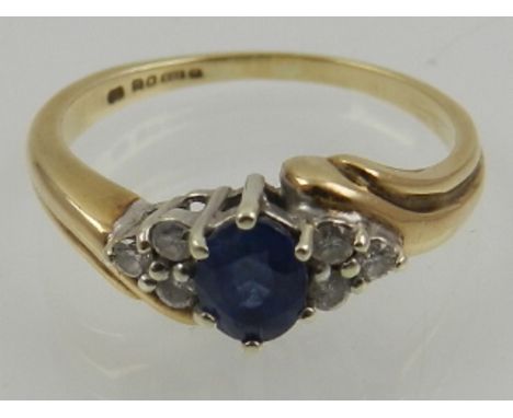 A 9 carat yellow gold, diamond, and sapphire crossover ring, set oval cut blue sapphire flanked by six round cut diamonds. 