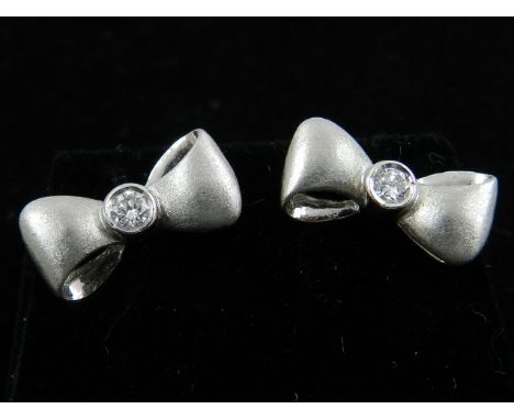 A pair of white metal and diamond set bow-shaped earrings. 
