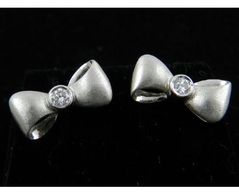 A pair of white metal and diamond set bow-shaped earrings. 