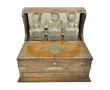 Edwardian oak tantalus with brass mounts and handles, the mirrored high-back with recess containing three square sided cut gl