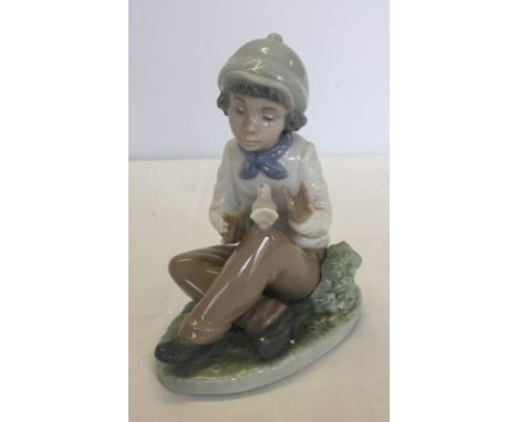 A boxed Nao porcelain figurine of a boy sitting with a dove. Model #1154, "Calming Caress". Approx. 15cm tall