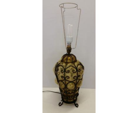 A vintage amber glass lamp base with black metal work overlay. Also has a light within the glass base. 