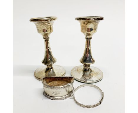 A pair of hallmarked silver candlesticks with a silver napkin ring and child's bangle.