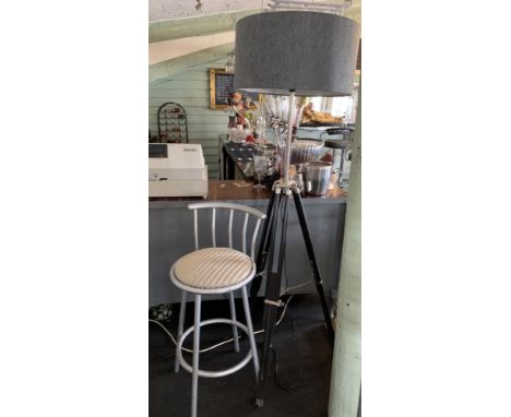 A chrome and black surveyors tripod style freestanding lamp with shade and a silver sprayed high swivel bar stool 