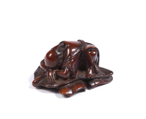 A Japanese wood netsuke of a farmer  19th Century  sleeping face down on a folded palm leaf, his head resting on his arms, un