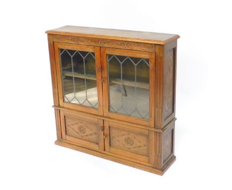 An Inglesants oak cupboard bookcase, with two glazed doors opening to reveal a single shelf, over a pair of carved cupboard d