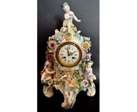 A Late 19th Early 20th Century German Porcelain Table Clock with putti cresting and with foliate encrusted decoration in poly