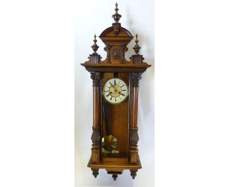 A 19th Century Walnut Vienna Wall Clock with a carved triple finial cresting, the enamel dial with two train movement strikin