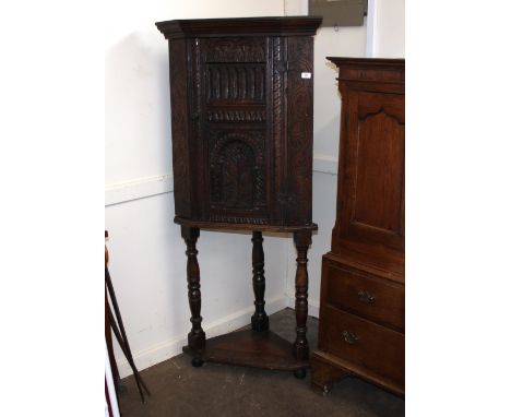 An Antique carved oak freestanding corner cupboard, fitted interior shelf and drawer, enclosed by a profusely carved panelled