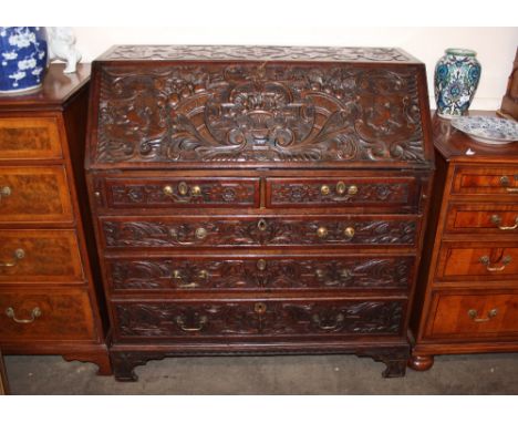 An Antique carved oak bureau, the fall front profusely decorated with cornucopia, flowers and rampant lions enclosing a fitte