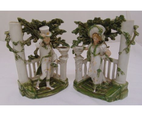 A pair of Staffordshire ceramic figurines of a lady and gentleman in formal attire in a leafy bower, 27cm (h)