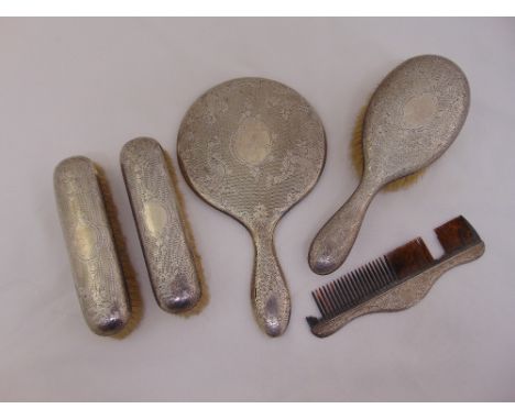 A silver dressing table set engraved with leaves and flowers comprising hand mirror, hairbrush, comb and two clothes brushes,