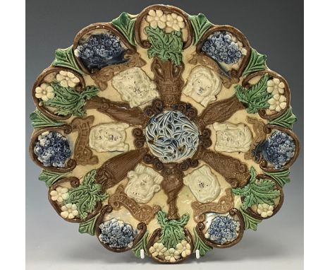 A Castle Hedingham pottery circular dish by Edward Bingham, decorated in relief with masks and vases of flowers, incised and 