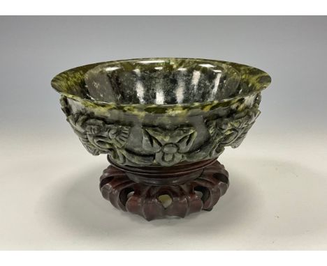 A Qing period Chinese spinach jade bowl on stand, flared rim, the sides carved with dragons, hardwood lotus leaf stand, 15cm 