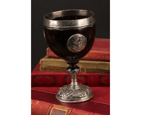 An 18th century silver mounted pedestal coconut cup, the ovoid bowl applied with portrait roundels, the rim engraved with hun