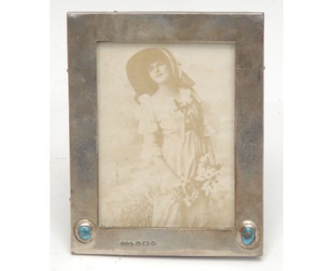 Liberty &amp; Co - a silver easel photograph frame, set with two Ruskin type turquoise roundels, Birmingham 1904, the apertur