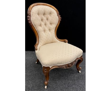 A Victorian carved walnut balloon-back nursing chair, button upholstered back, sprung seat, cabriole legs, with ceramic caste