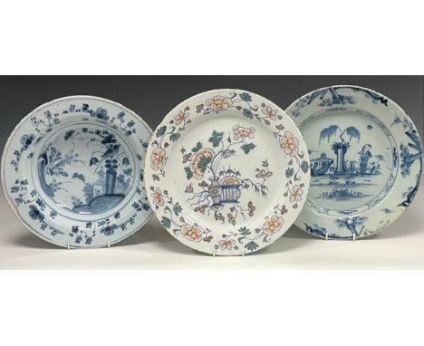 A 18th century English Delftware plate, decorated with vases on plinth, peonies and twining vines, the rim with sprigs of sim