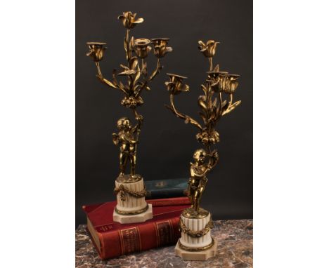 A pair of 19th century gilt metal candelabra, each cast as a scantily clad putto holding flowering branches, white marble flu